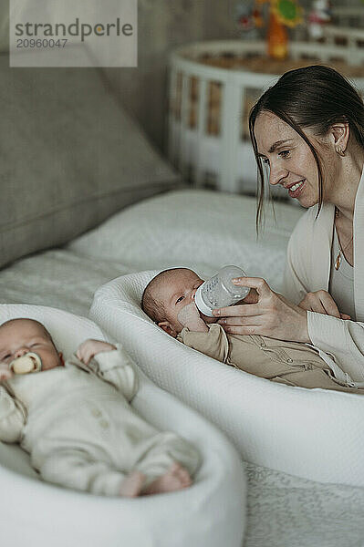 Mother feeding son lying near brother on bed at home