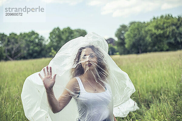 Young woman wrapped in polythene on field