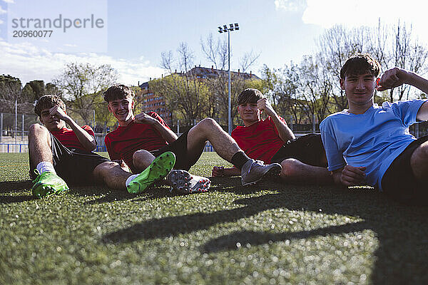 Happy soccer players sitting together on field under sky