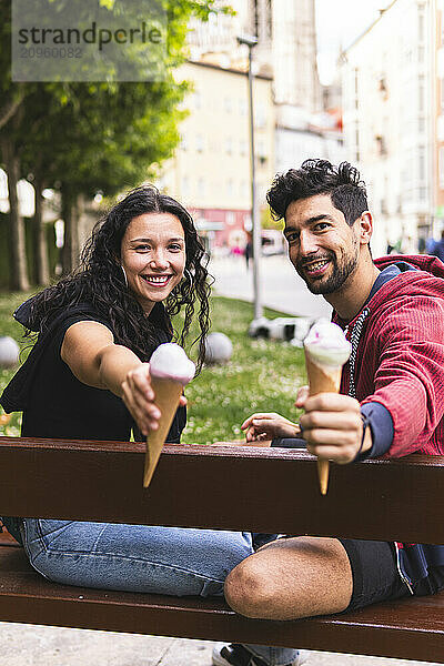 Happy couple showing ice cream and sitting on bench