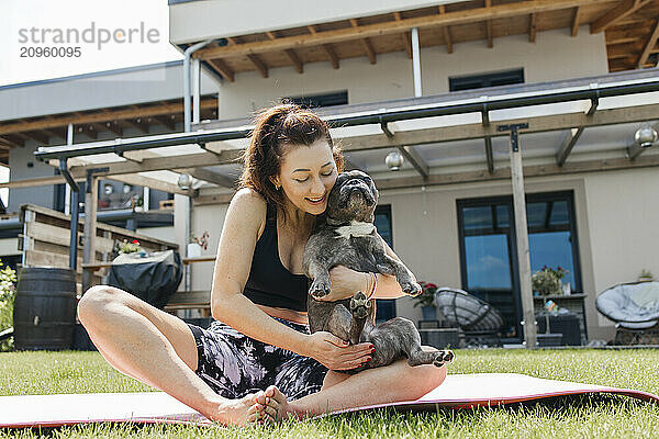 Mature woman playing with dog and sitting on exercise mat in back yard