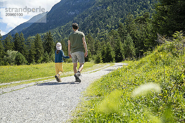 Father and daughter hiking on footpath near mountain