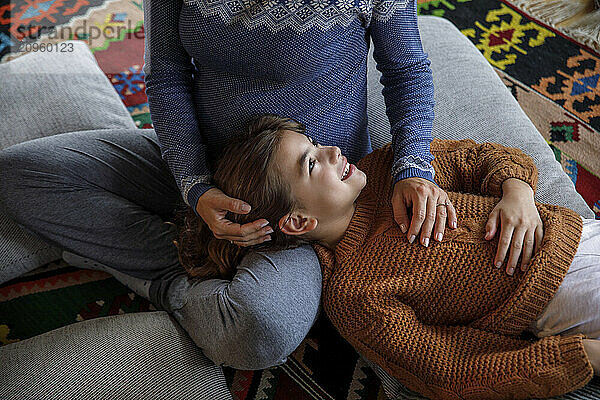 Smiling daughter resting head on mother's lap at home