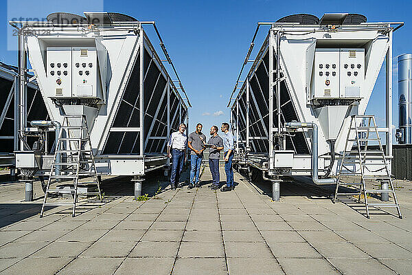 Businessmen and employees having a meeting on rooftop beside refrigeration installation