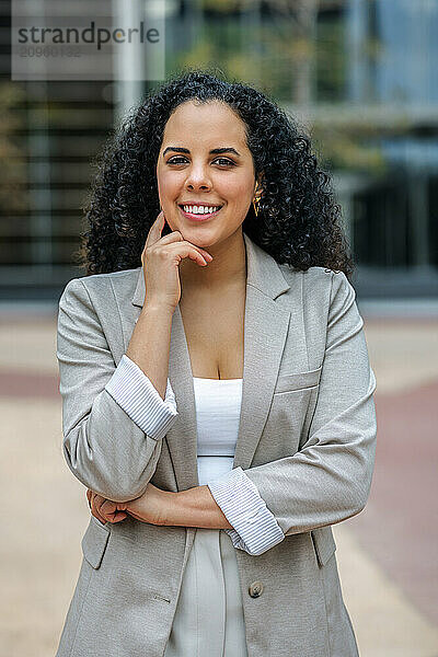 Smiling businesswoman with hand on chin standing near office