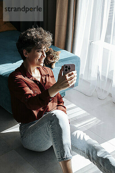 Happy woman taking selfie with cat at home