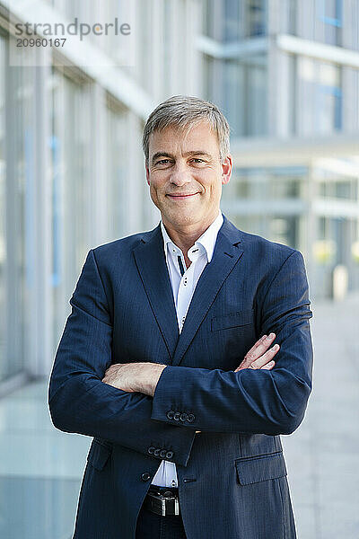 Confident businessman standing in office building with arms crossed