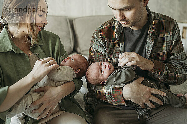 Parents carrying newborn babies in arms and sitting at home