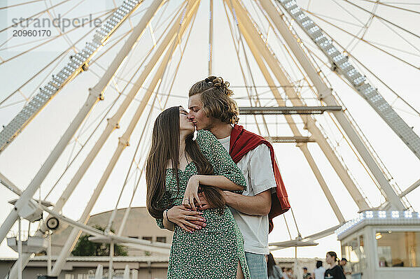 Happy couple kissing each other standing in front of ferris wheel