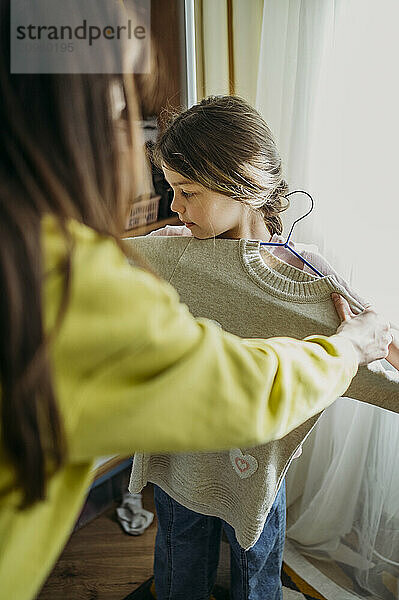 Mother trying sweater on daughter at home