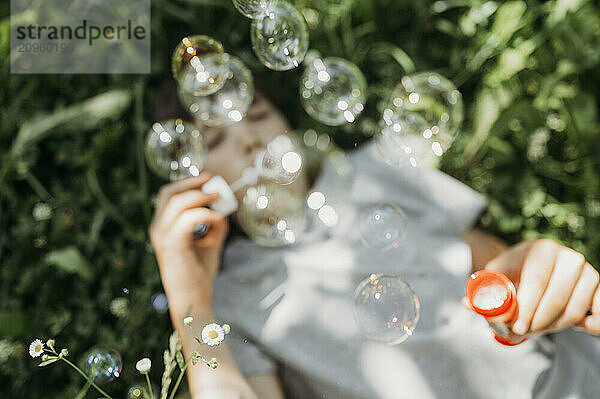 Boy lying on back and blowing bubbles at park