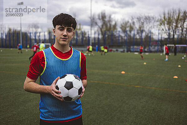 Smiling teenage soccer player standing with ball on field