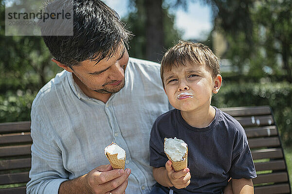 Boy eating ice cream with father in public park