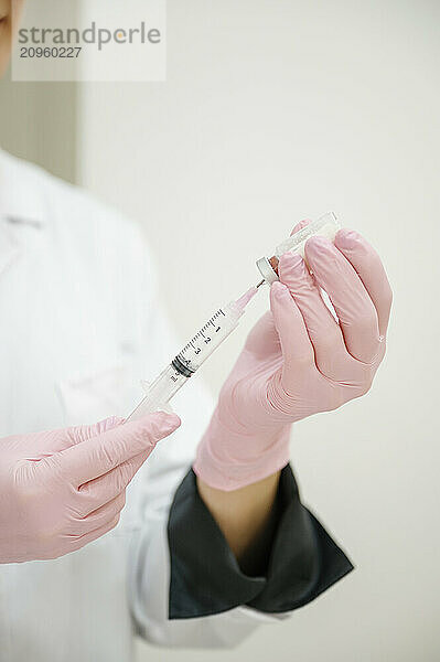 Cosmetologist wearing glove and filling syringe through vial at clinic