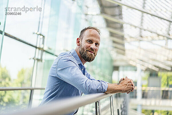 Confident businessman staning in office building leaning on railing