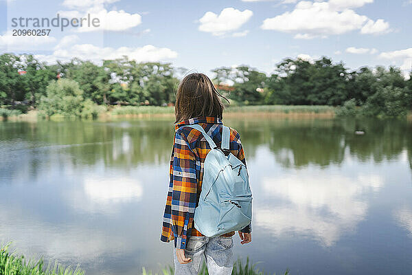 Boy with backpack standing near lake