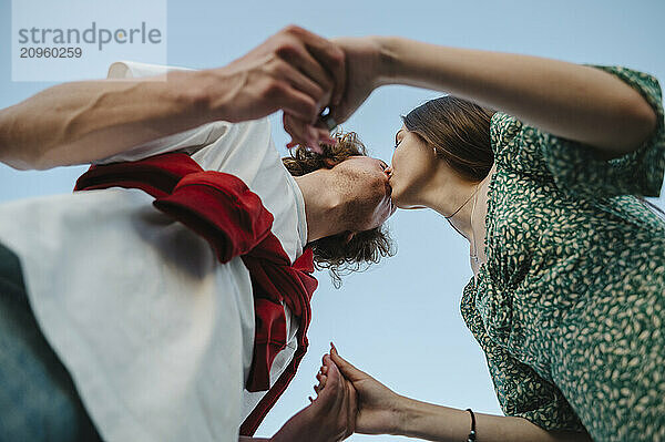 Romantic couple holding hands and kissing under blue sky