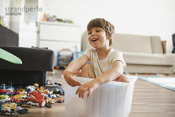 Smiling boy sitting in plastic container and having fun at home