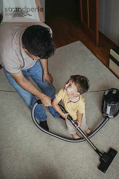 Father and son using vacuum cleaner and cleaning carpet at home