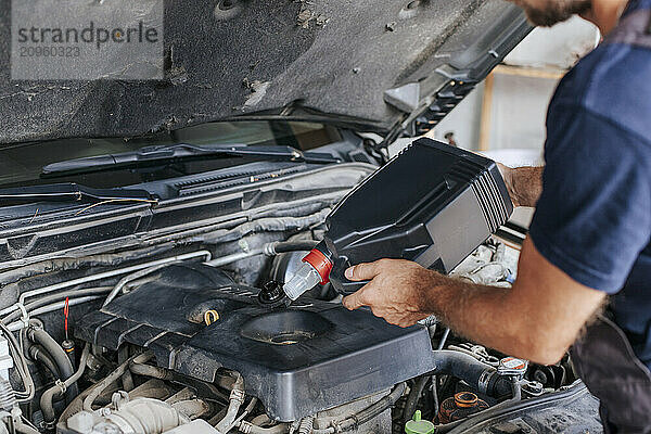 Man pouring liquid in car engine inside garage