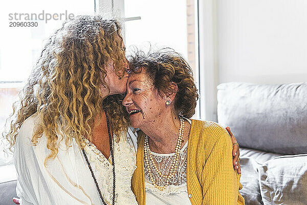 Daughter kissing mother on forehead at home