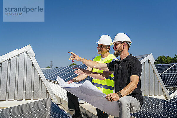 Two solar technicians discussing installation plan on the rooftop of a company building with solar panels.