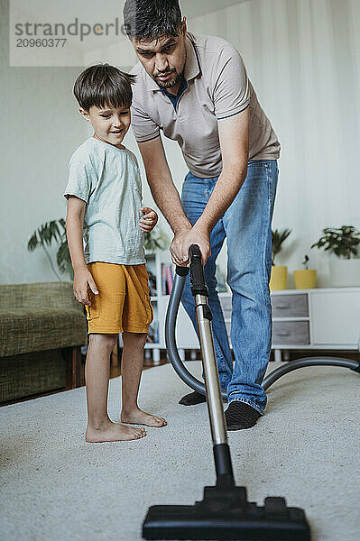 Father and son vacuuming carpet at home