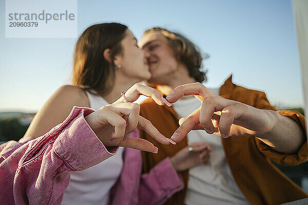 Happy couple kissing and gesturing heart shape on sunny day