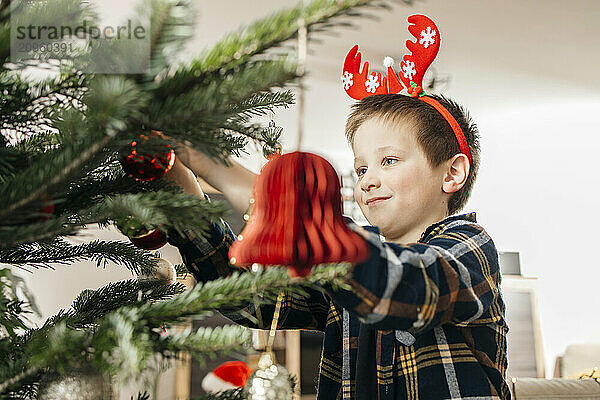 Boy with antlers decorating Christmas tree at home