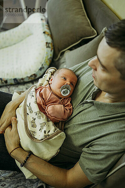 Father holding baby girl and sitting on sofa at home