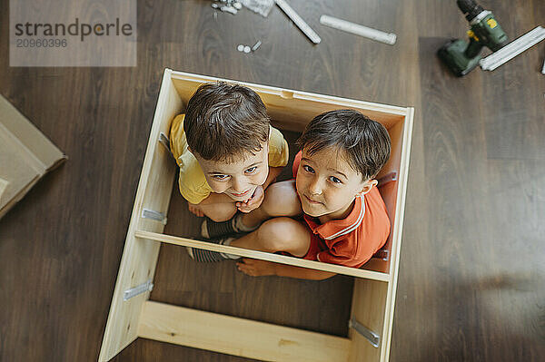 Smiling boys inside wooden shelf at home