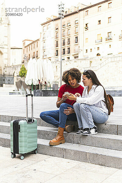 Friends sitting on steps and using smart phone at street