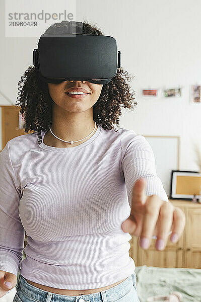 Smiling girl wearing virtual reality simulators gesturing at home