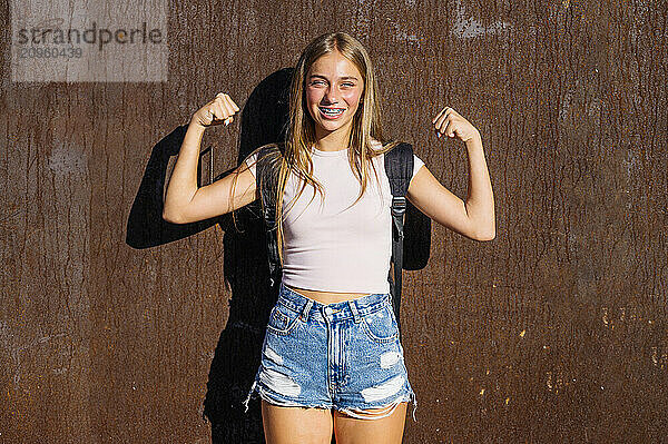 Smiling girl flexing muscles and standing near wall