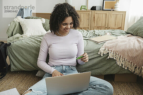 Happy curly haired girl making payment through credit card at home