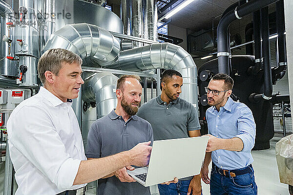 Businessmen and employees with laptop having a meeting in factory