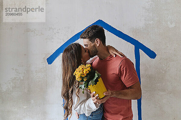 Couple kissing and holding flower bouquet in front of wall at site