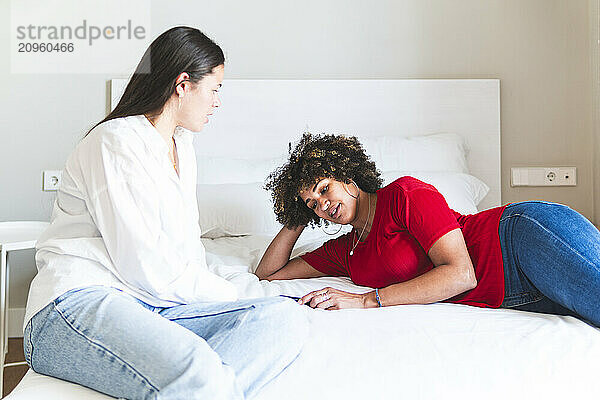 Woman lying near friend and discussing at hotel room