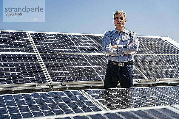 A self-assured male executive standing proudly in the midst of a field of solar panels