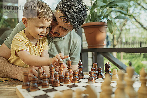 Happy father sitting with son playing chess on porch