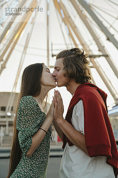 Romantic couple kissing each other standing in front of ferris wheel at amusement park