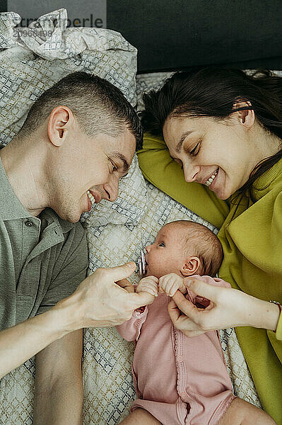 Happy parents holding daughter's hand and lying on bed