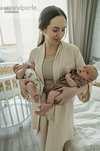 Mother holding twins in bedroom at home