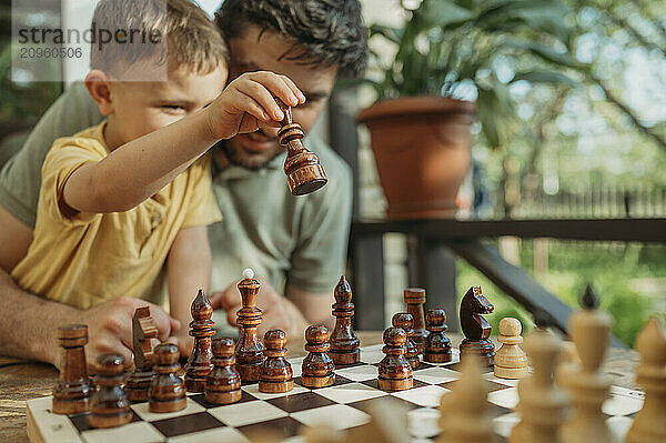 Son playing chess with father on porch