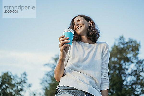 Happy woman holding disposable cup of coffee in garden