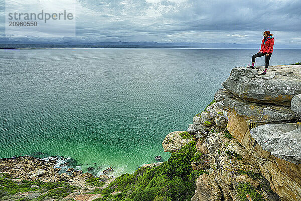 Woman standing on edge of cliff and looking at ocean in Robberg Nature Reserve  Garden Route National Park  Western Cape  South Africa