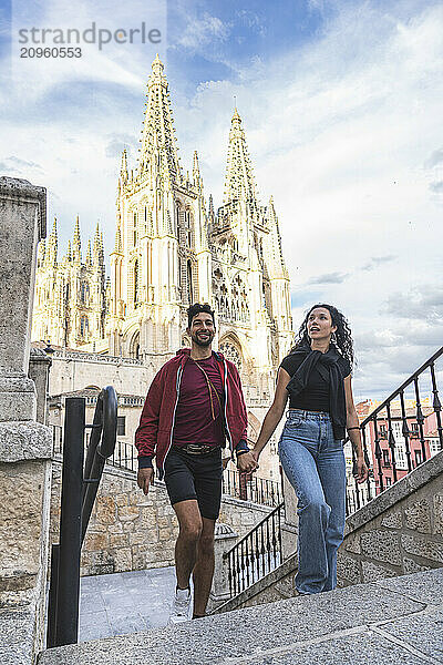 Couple holding hands and moving up on stairs in front of Burgos Cathedral