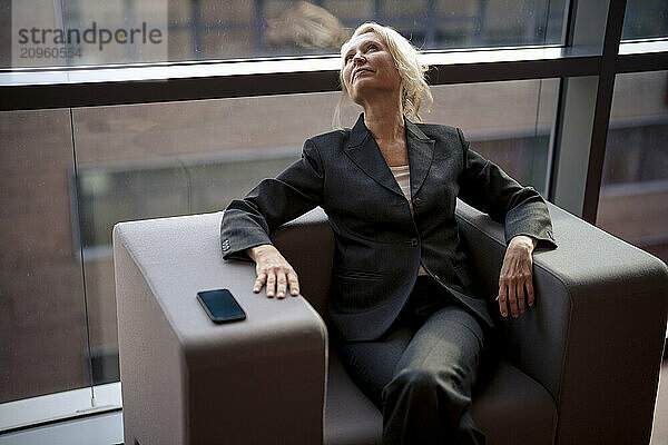 Thoughtful businesswoman looking up sitting on chair at office