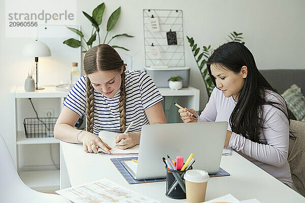 Students working on homework and sitting near table with laptop at home