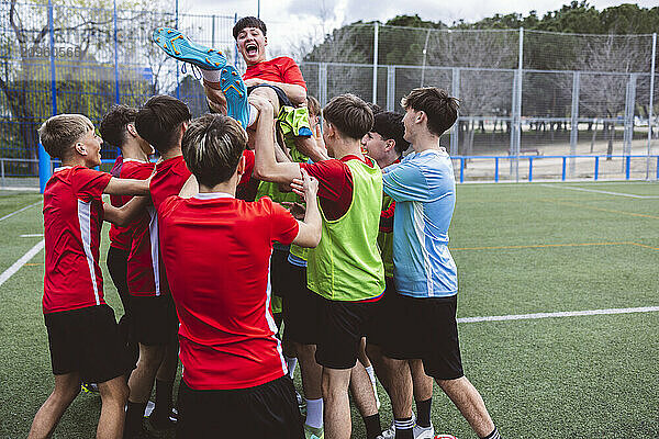 Happy soccer team picking up player and celebrating on field